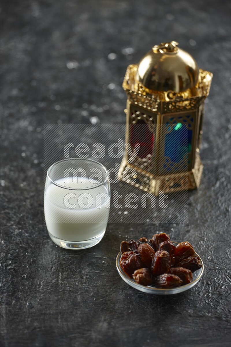 A golden lantern with different drinks, dates, nuts, prayer beads and quran on textured black background