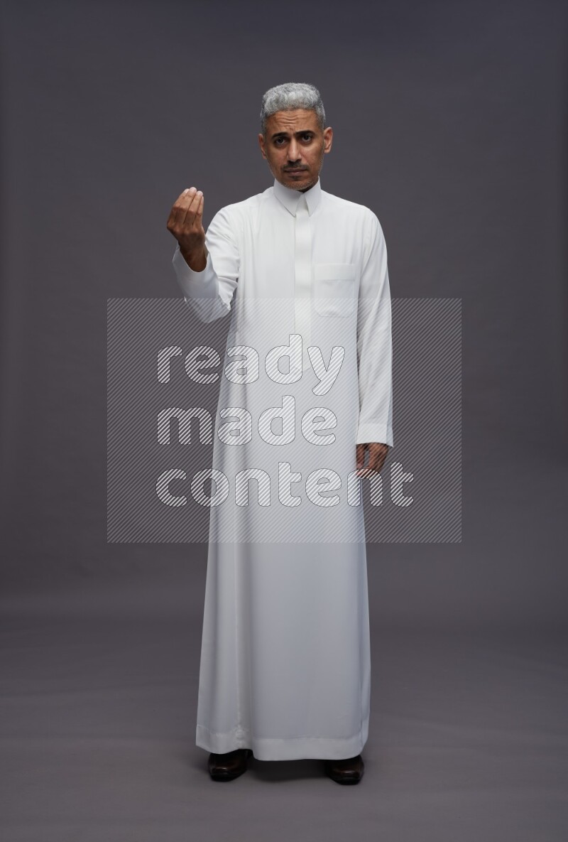 Saudi man wearing thob standing interacting with the camera on gray background