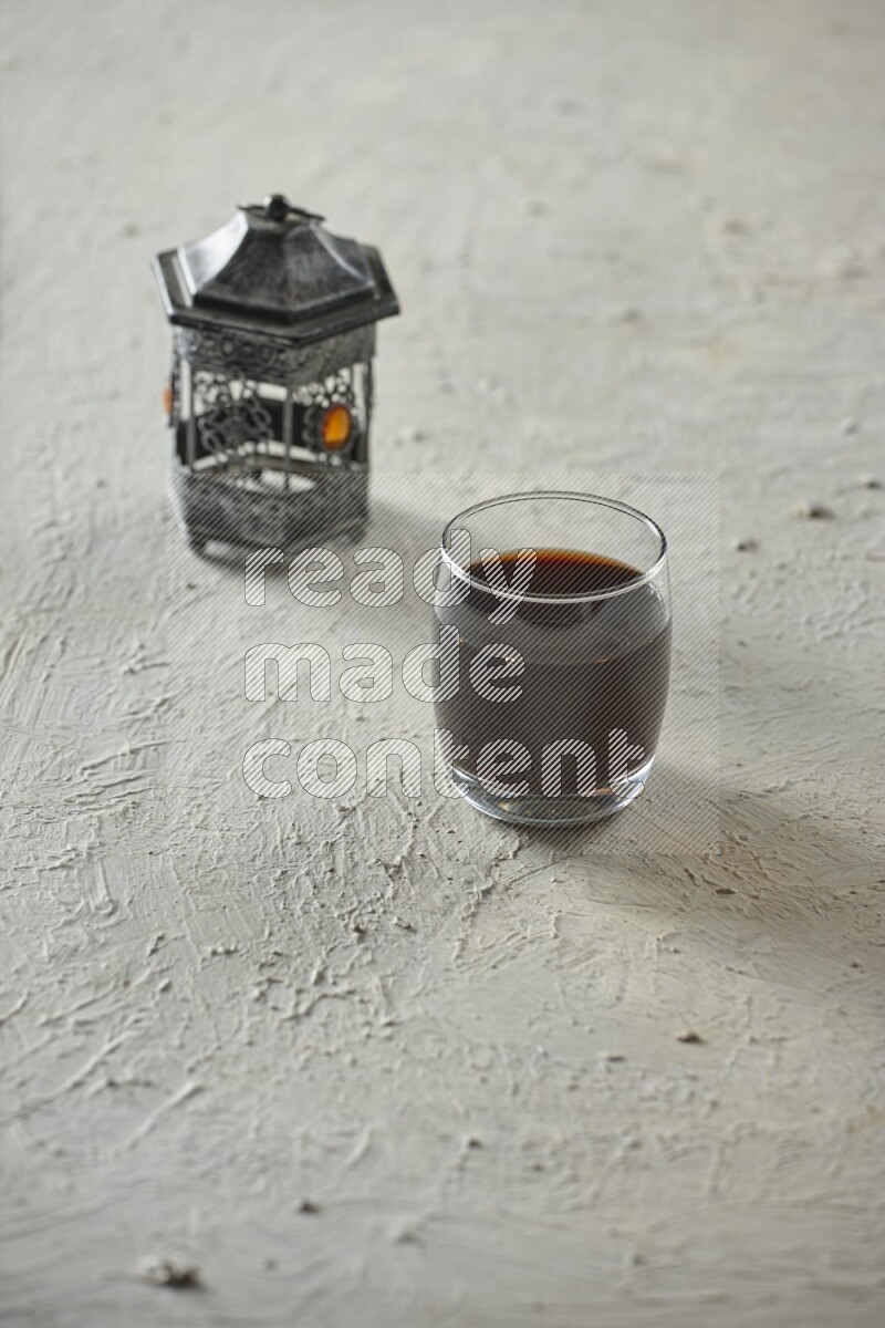 A silver lantern with different drinks, dates, nuts, prayer beads and quran on textured white background