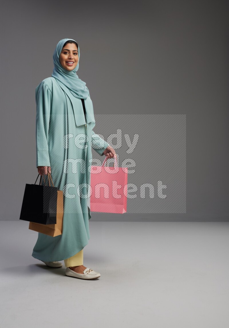 Saudi Woman wearing Abaya standing holding shopping bag on Gray background