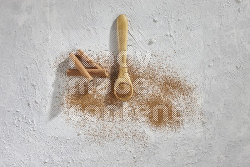 Cinnamon powder in a wooden spoon with cinnamon sticks and sprinkles powder on the flooring on white background