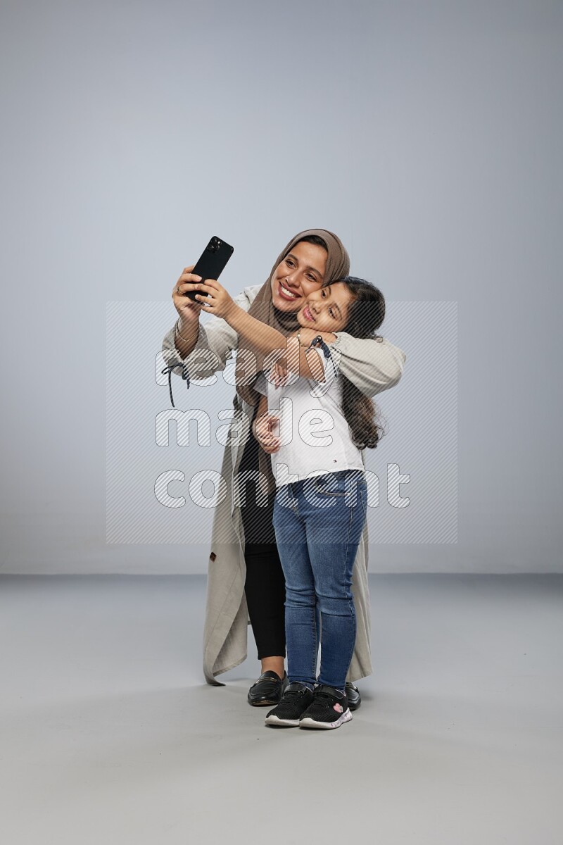 A girl standing taking selfie with her mother on gray background