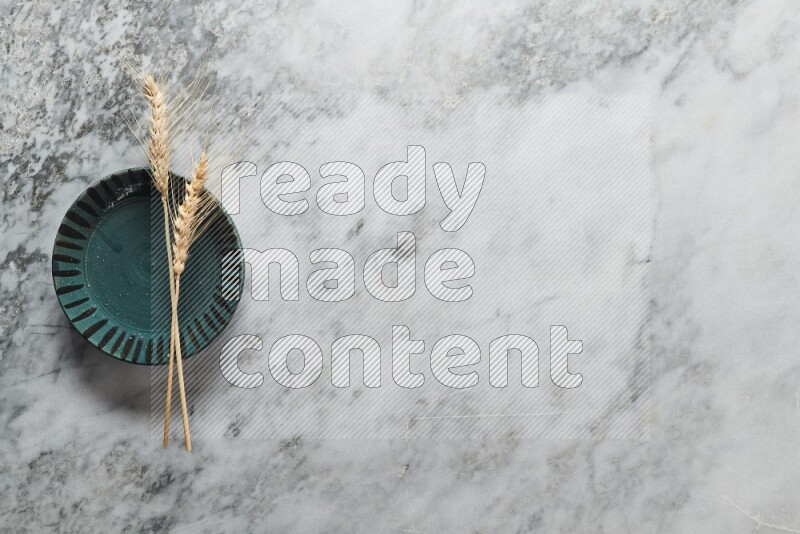 Wheat stalks on multicolored pottery plate on grey marble background