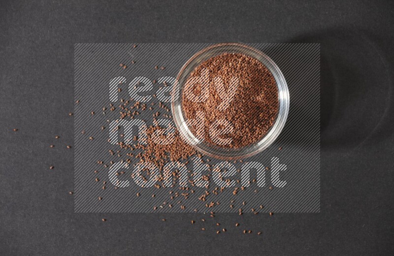 وعاء زجاجي ممتلئ ببذور حب الرشاد محاط بالبذور على أرضية سوداء