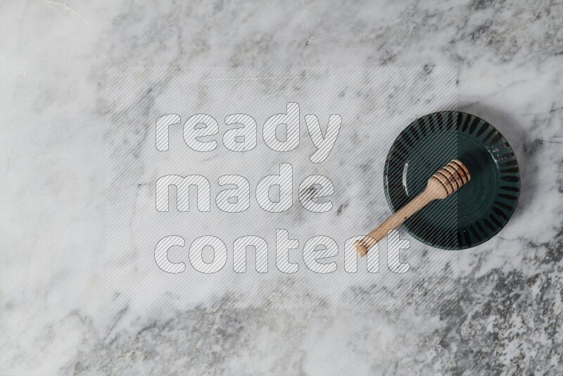 Multicolored pottery plate with wooden honey dipper in it on grey marble background