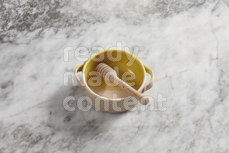 Multicolored pottery bowl with wooden honey dipper in it on grey marble background