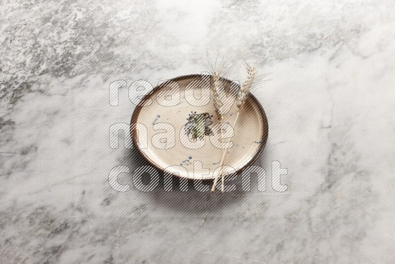 Wheat stalks on decorative pottery plate on grey marble background