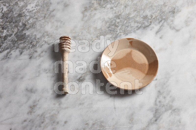 Multicolored pottery plate with wooden honey dipper on the side on grey marble background