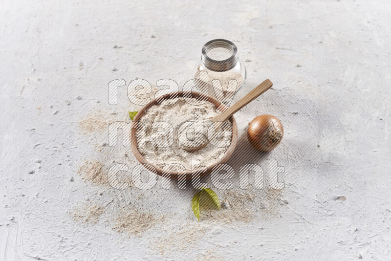 A wooden bowl full of onion powder with a glass jar beside it and fresh onion on white background