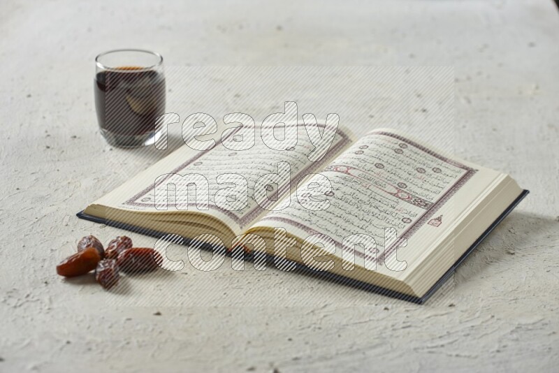 Quran with dates, prayer beads and different drinks all placed on textured white background