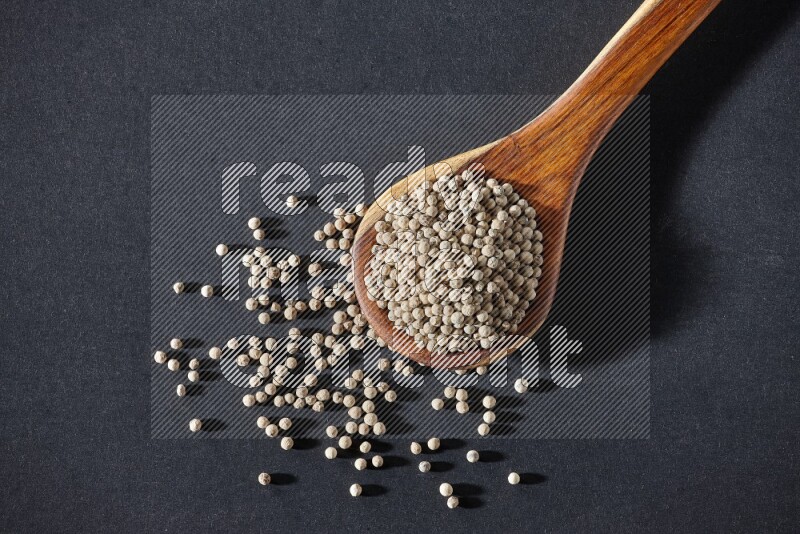 A wooden ladle full of white pepper beads on black flooring
