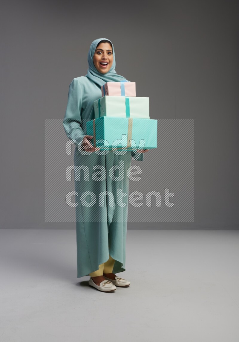 Saudi Woman wearing Abaya standing holding gift box on Gray background