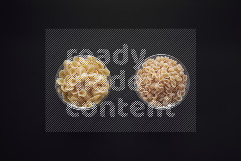 Different pasta types in glass bowls on black background