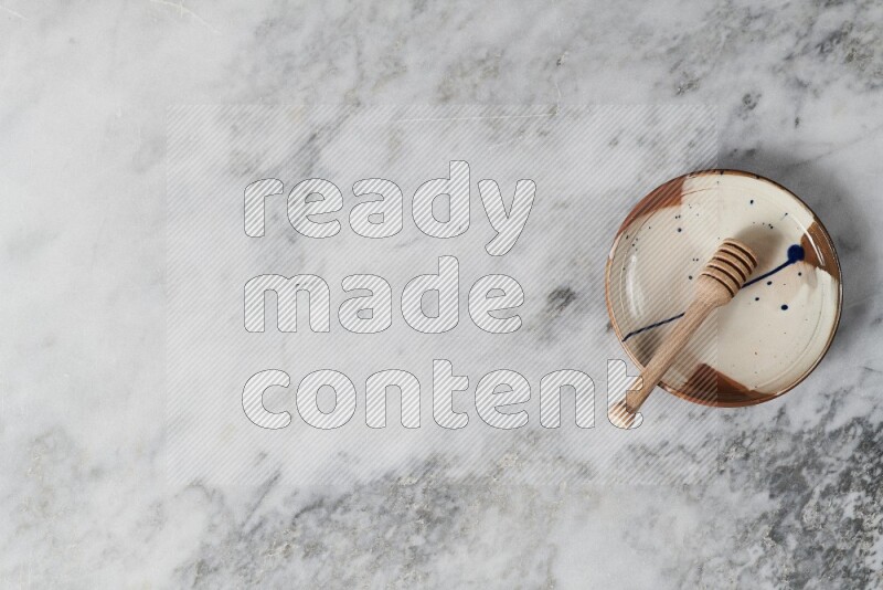 Multicolored pottery plate with wooden honey dipper in it on grey marble background