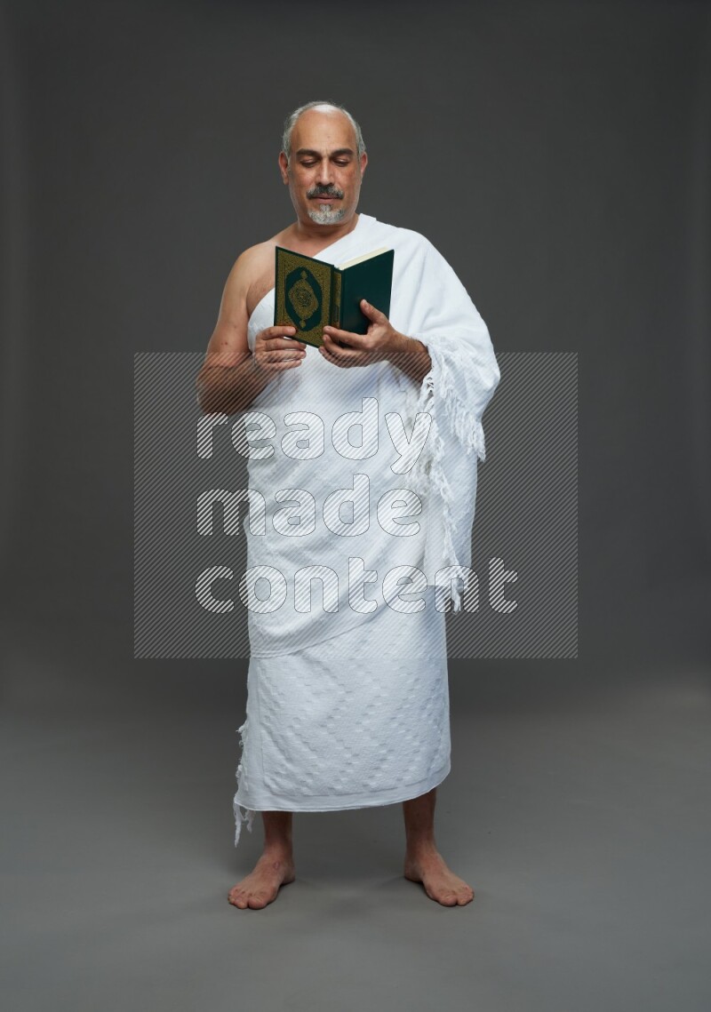 A man wearing Ehram Standing reading quran on gray background