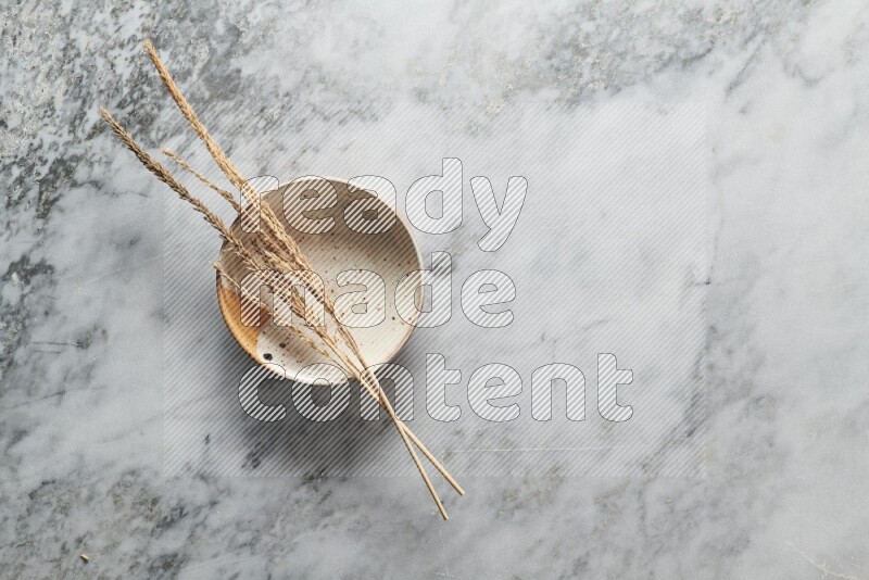 Wheat stalks on multicolored pottery plate on grey marble background