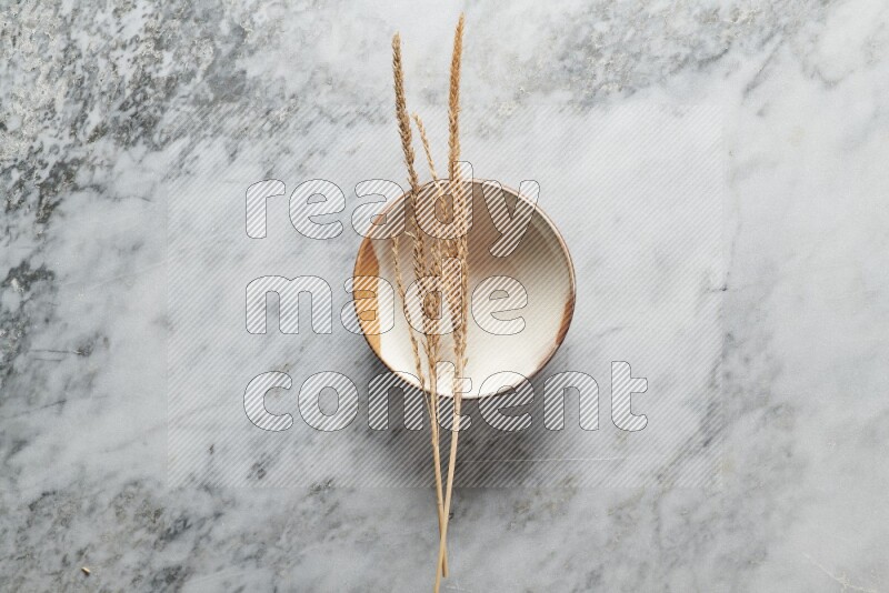 Wheat stalks on multicolored pottery plate on grey marble background