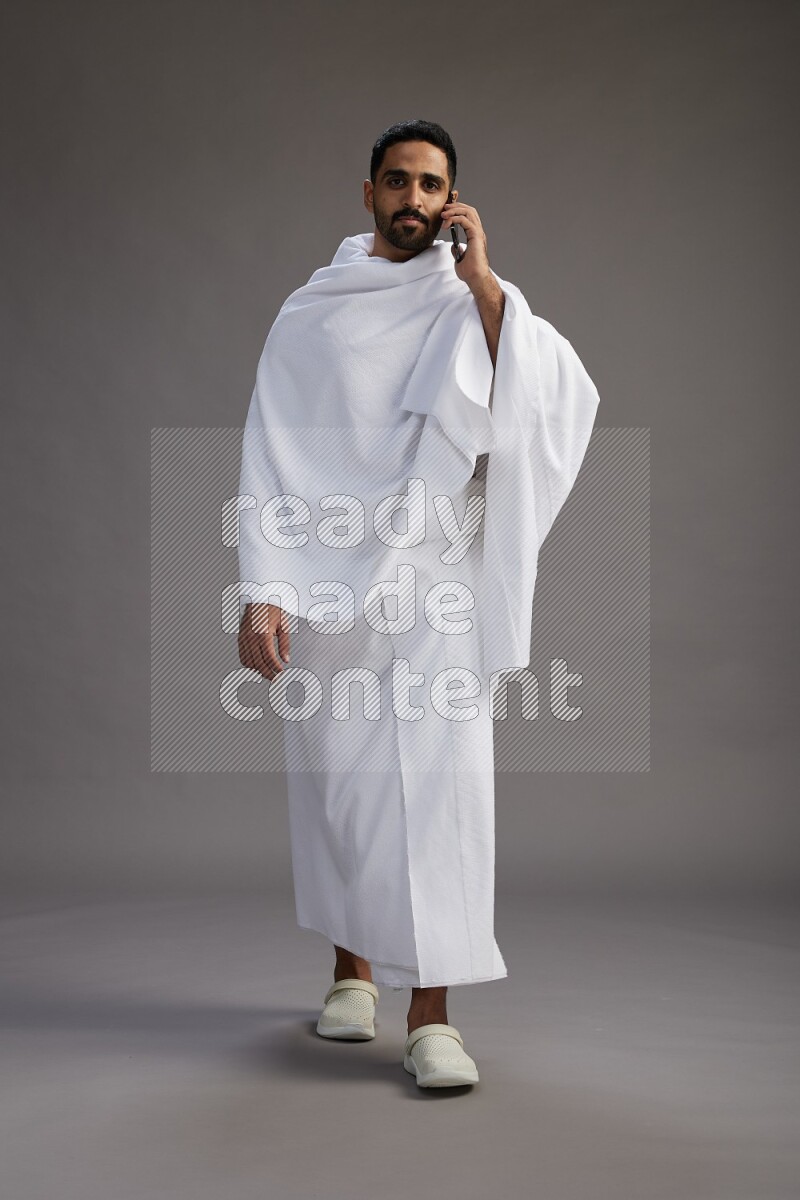 A man wearing Ehram Standing talking on phone on gray background