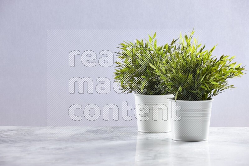 Two green artificial plants in white pot on grey marble background