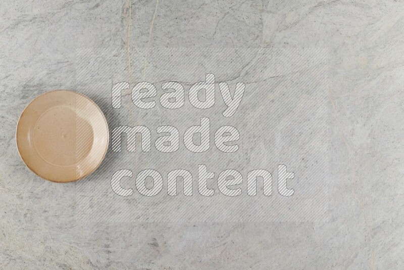 A circular beige pottery plate on grey marble background