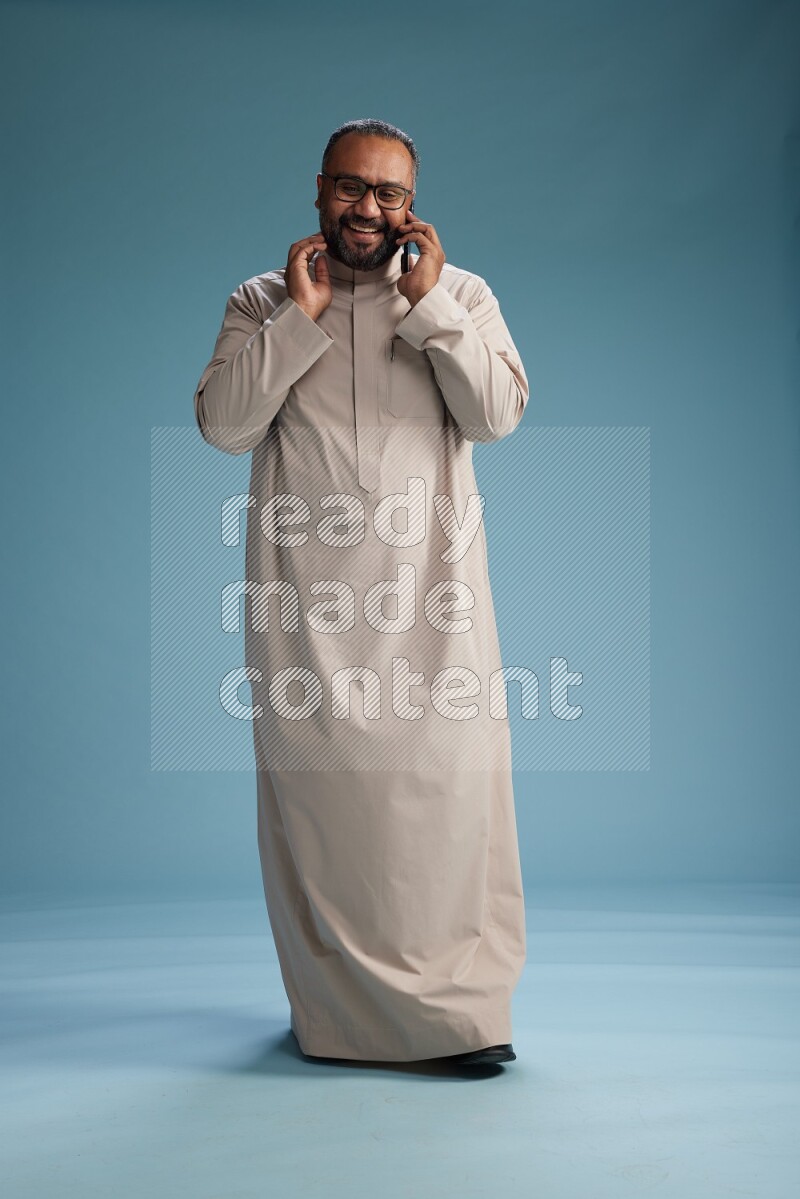 Saudi Man without shimag Standing talking on phone on blue background