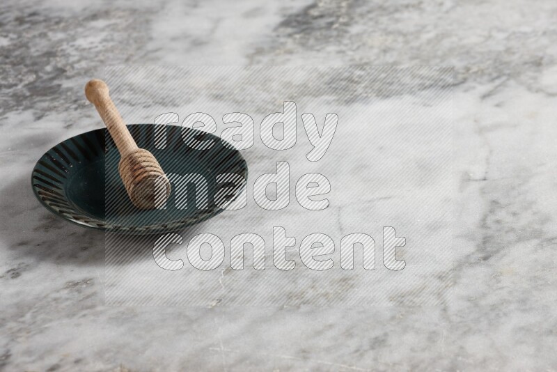 Multicolored pottery plate with wooden honey dipper in it on grey marble background