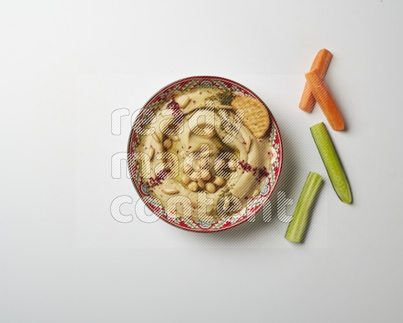 Hummus in a red plate with patterns garnished with zaatar & sumak on a white background
