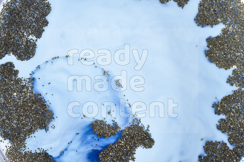 A close-up of sparkling gold glitter scattered on swirling blue background