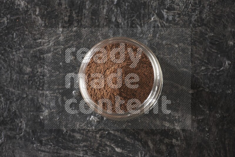 وعاء زجاجي ممتلئ ببودرة القرنفل على أرضية سوداء