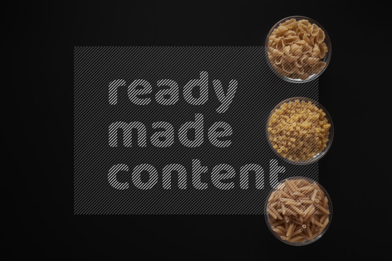 Different pasta types in 3 glass bowls on black background