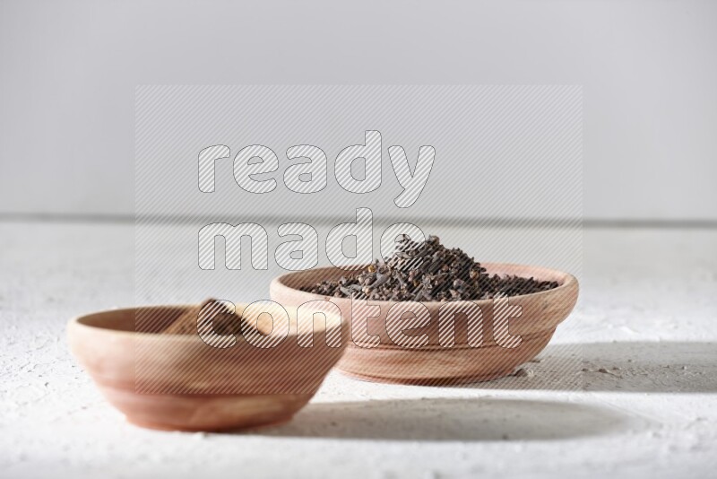 2 wooden bowls full of cloves powder and whole cloves on a textured white flooring