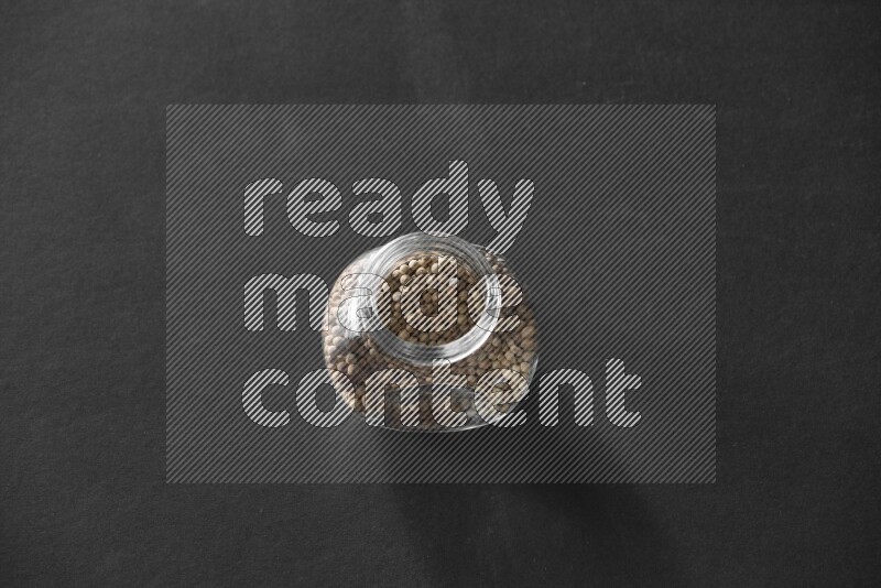 A glass spice jar full of white peppers on black flooring