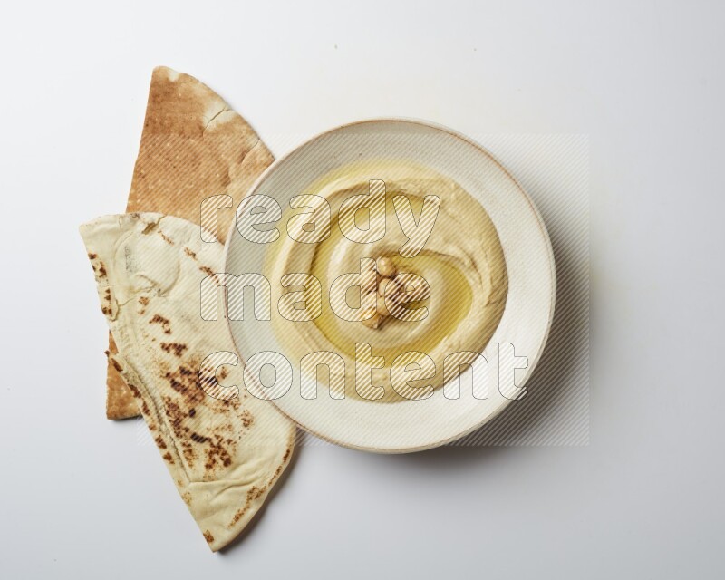 Hummus in a pottry plate garnished with roasted chickpeas on a white background
