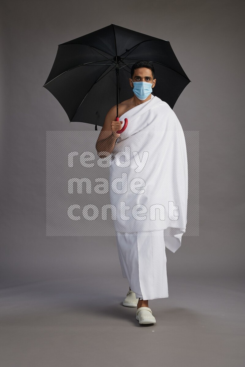 A man wearing Ehram and mask Standing holding umbrella on gray background on gray background