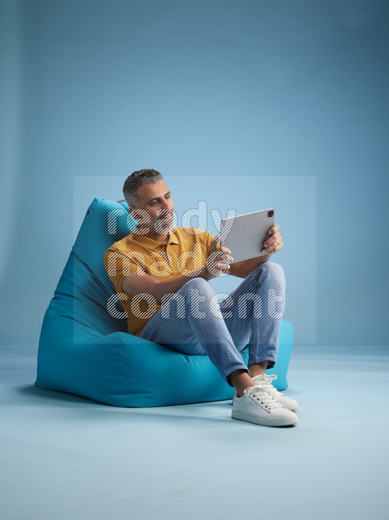 A man sitting on a blue beanbag and working on tablet