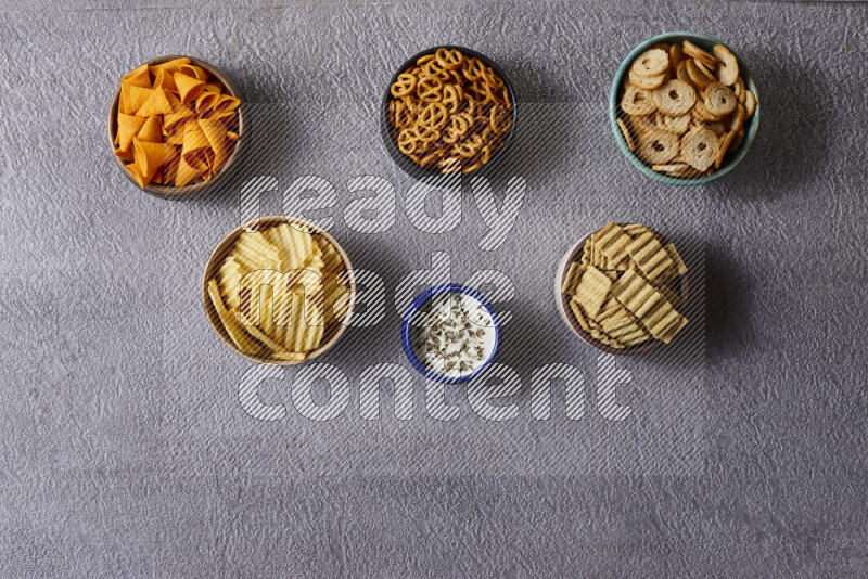 Assorted snacks in pottery bowls on grey background