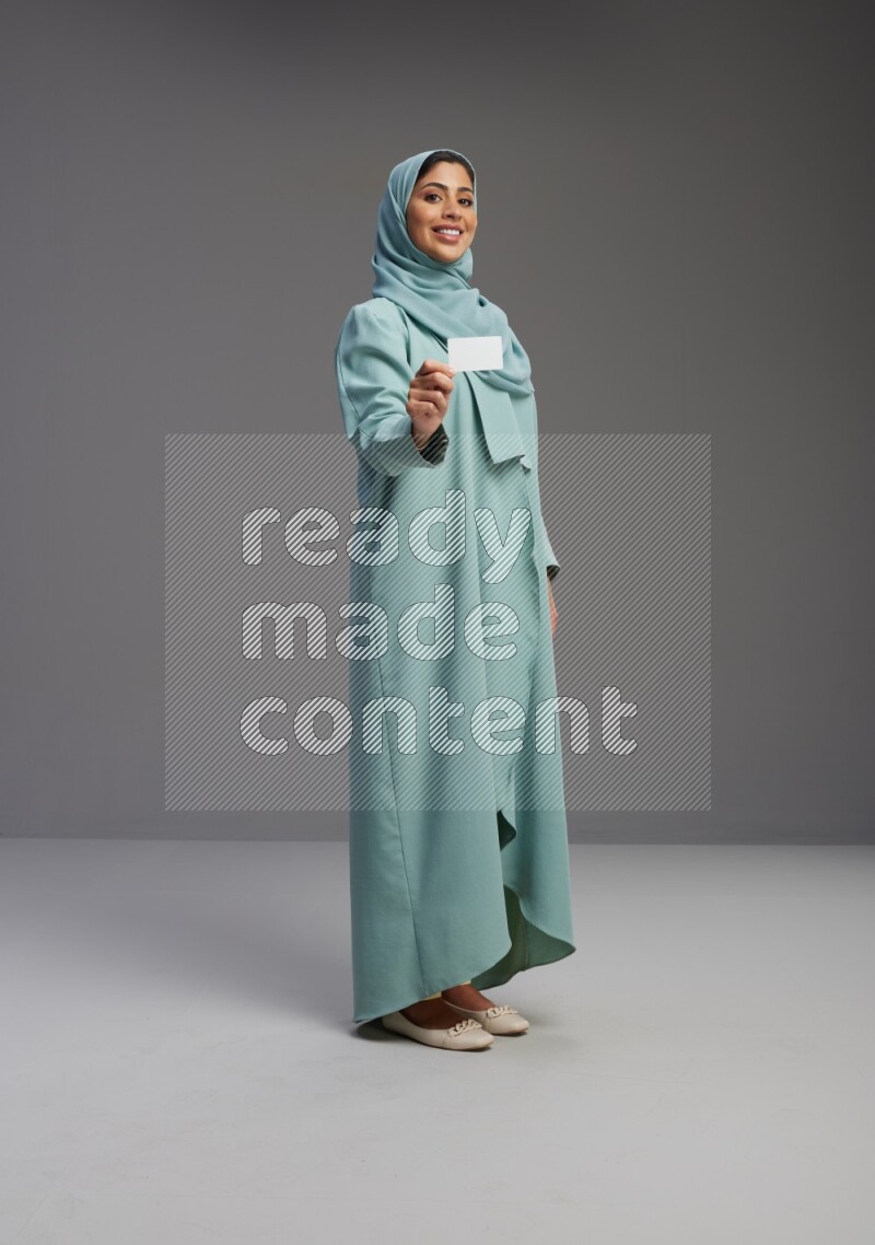 Saudi Woman wearing Abaya standing holding ATM card on Gray background