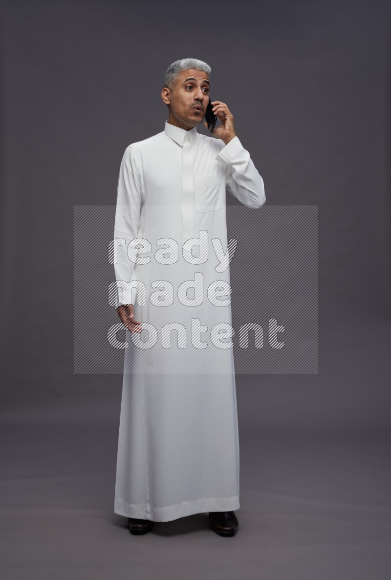 Saudi man wearing thob standing talking on phone on gray background