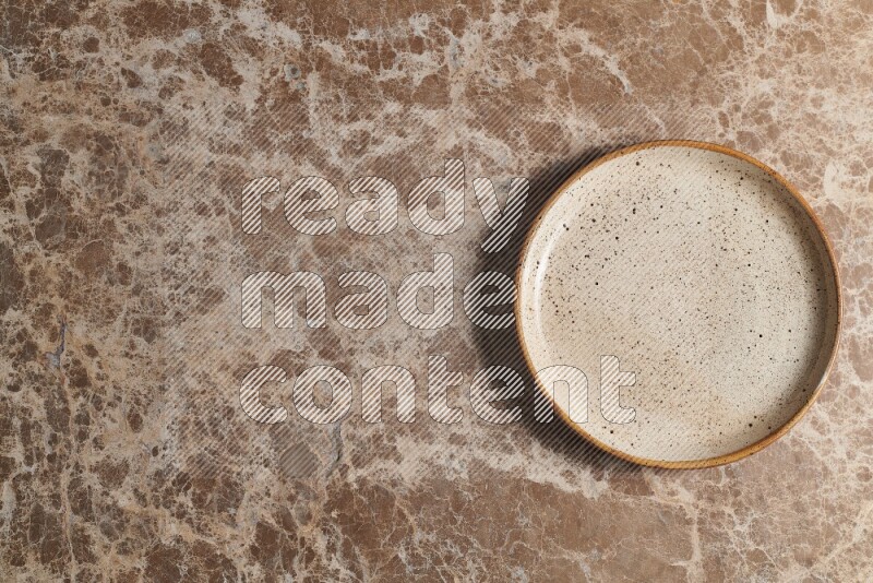 A beige pottery plate on beige marble background