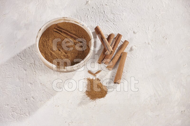 Ceramic bowl full of cinnamon powder with cinnamon sticks on the side on white background