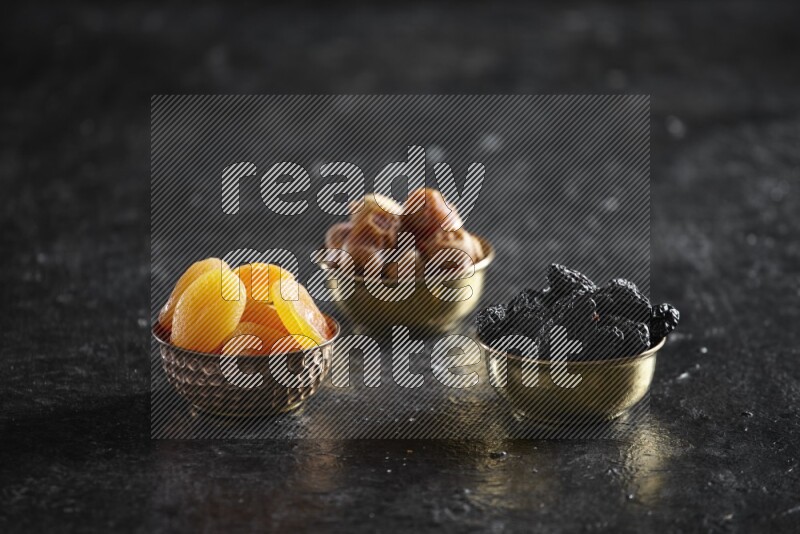 Dried fruits in metal bowls in a dark setup