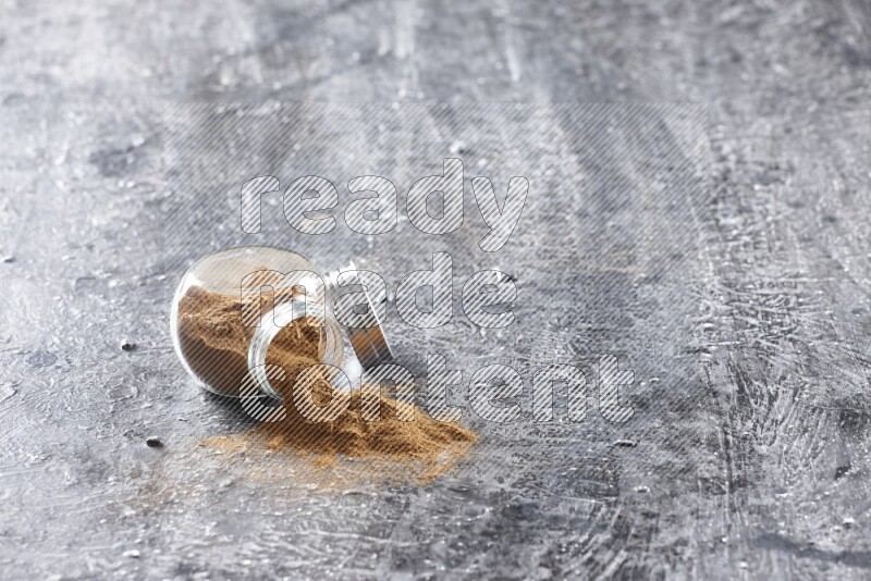Flipped herbal glass jar full of cinnamon powder on textured black background