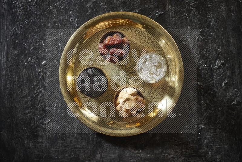 Dried fruits in metal bowls with water on a tray in dark setup
