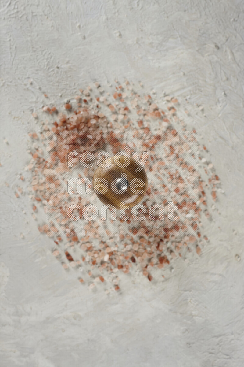 A wooden grinder standing upright and surrounded by coarse pink himalayan salt on white background