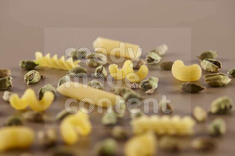Raw pasta with different ingredients such as cherry tomatoes, garlic, onions, red chilis, black pepper, white pepper, bay laurel leaves, rosemary and cardamom on beige background