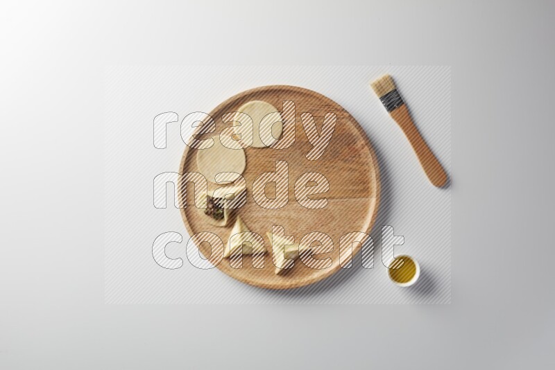two closed sambosas and one open sambosa filled with meat while oil with oil brush aside in a wooden dish on a white background