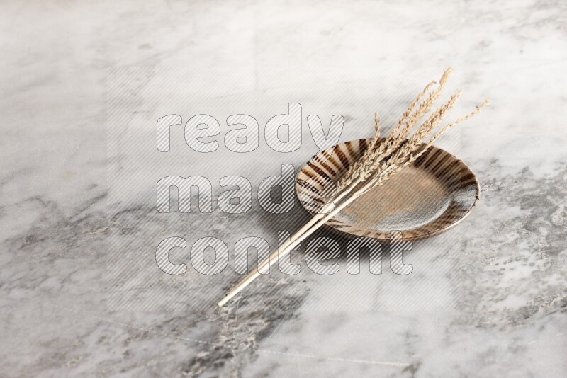 Wheat stalks on multicolored pottery plate on grey marble background