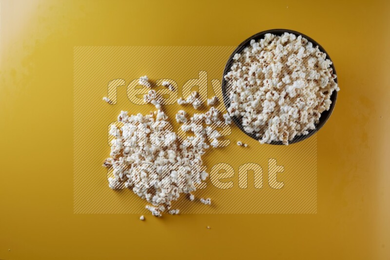A copper ceramic bowl full of popcorn with popcorn beside it on a yellow background in different angles