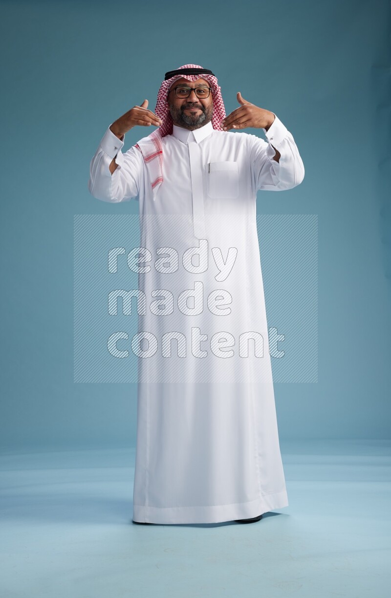 Saudi Man with shimag Standing Interacting with the camera on blue background