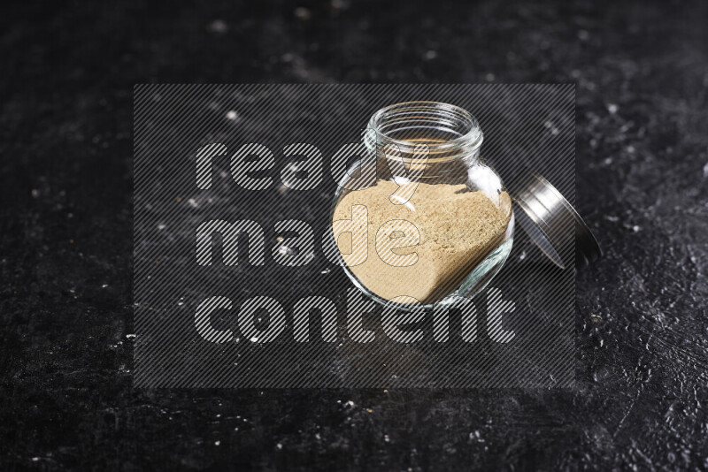 A glass jar full of ground ginger powder on black background
